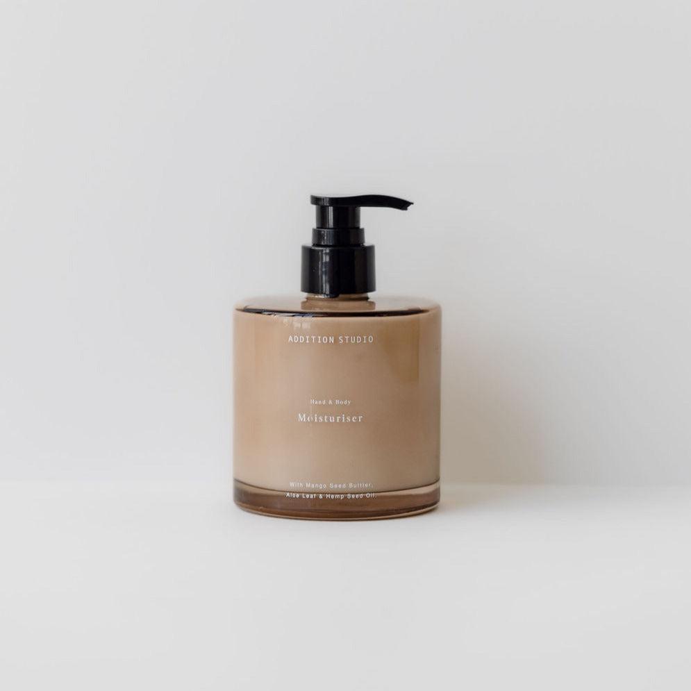 An all-natural Addition Studio hand & body moisturiser with a black pump on a white background.