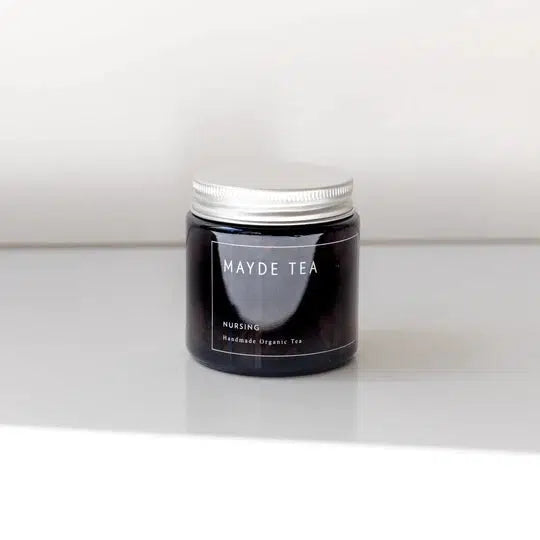 A jar of Mayde Tea nursing tea labeled "healthy lactation, handmade & organic tea" sits on a white surface against a light background.