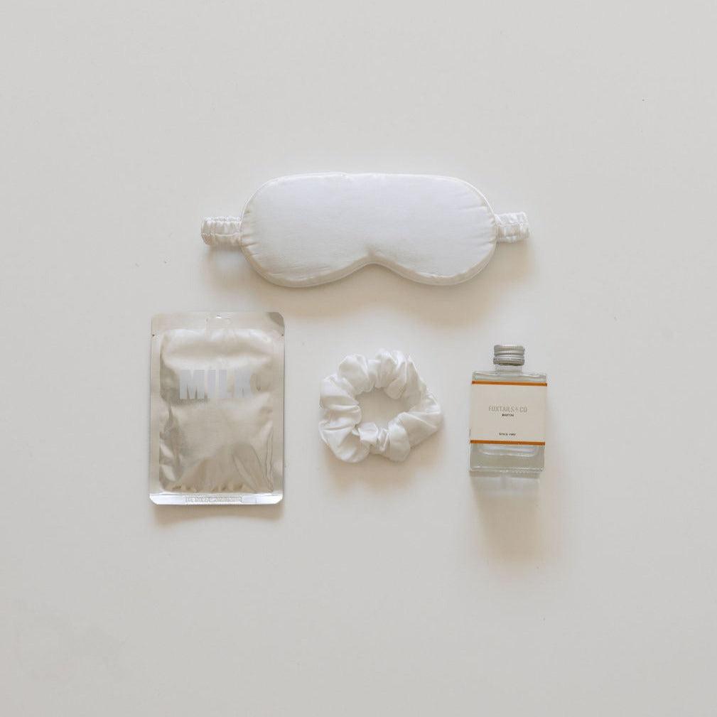 A "unwind hour" eye mask for relaxation and a bottle of water on a white surface by biglittlegifting.