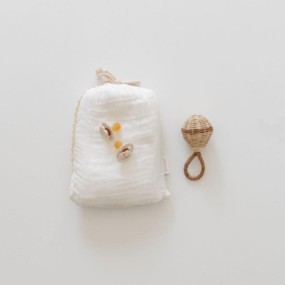 A white bag with a biglittlegifting wooden rattle next to it.