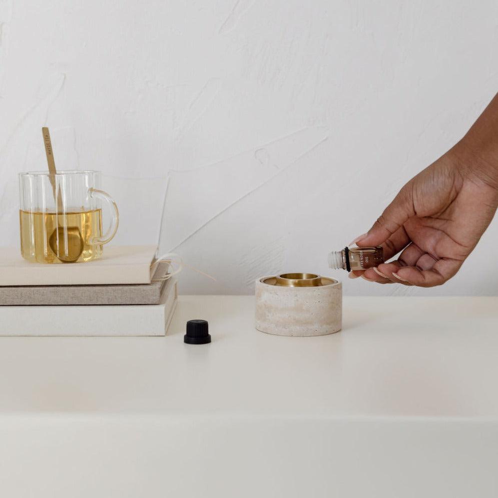 A person is holding an Addition Studio asteroid oil burner and a travertine book on a table.