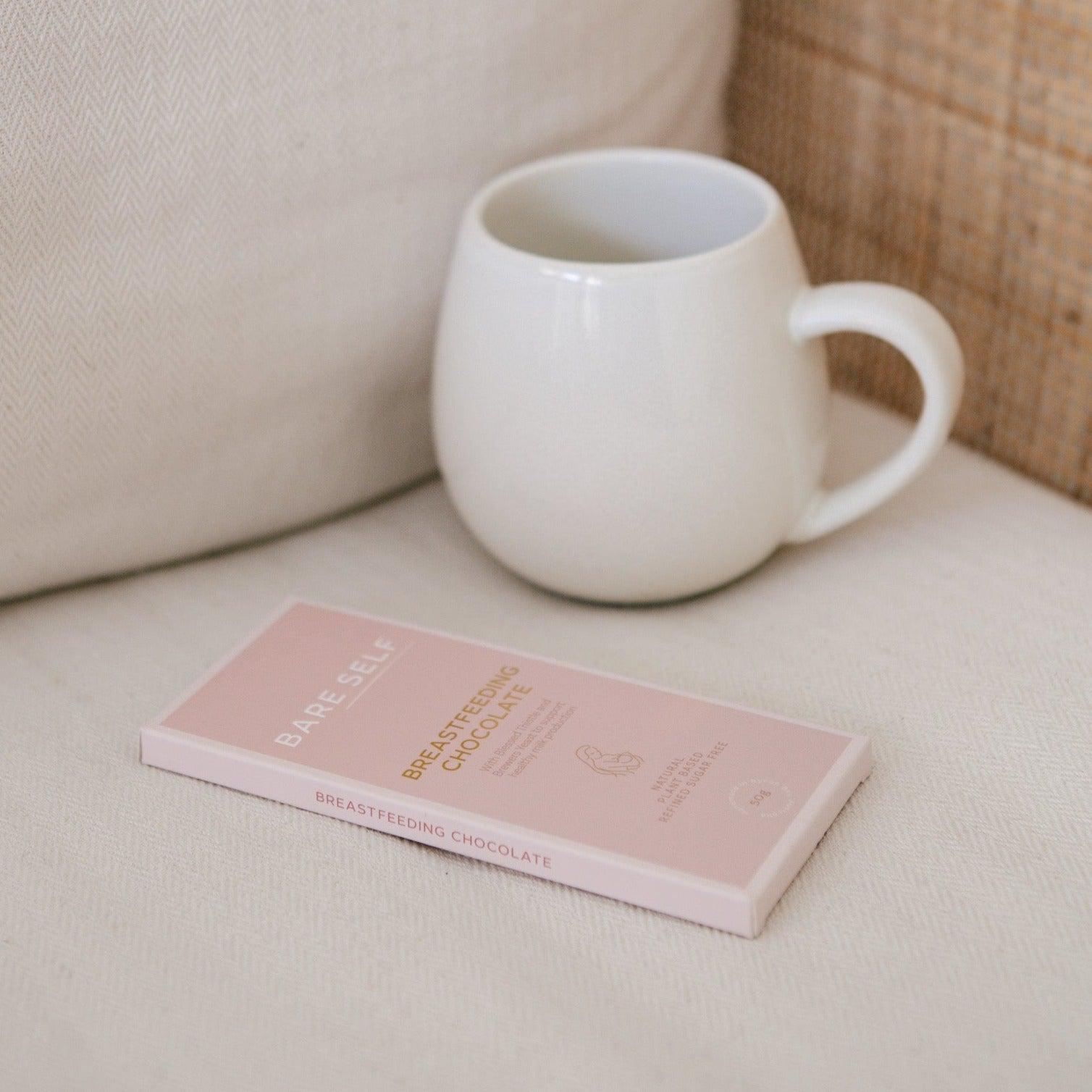 A cup of coffee from Bare Self and a breastfeeding chocolate bar from Bare Self on a white couch.