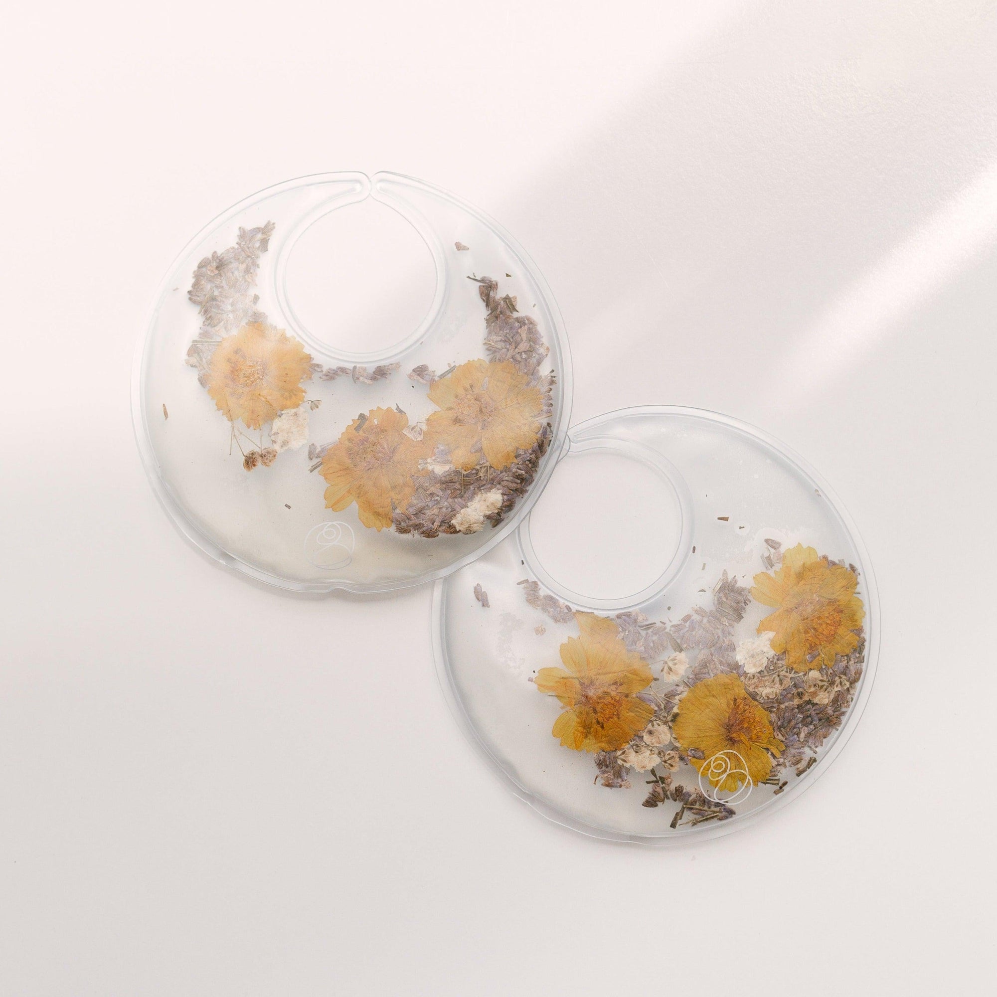 A pair of Breast Warm & Cool Insert earrings by Bare Mum with dried flowers on them.