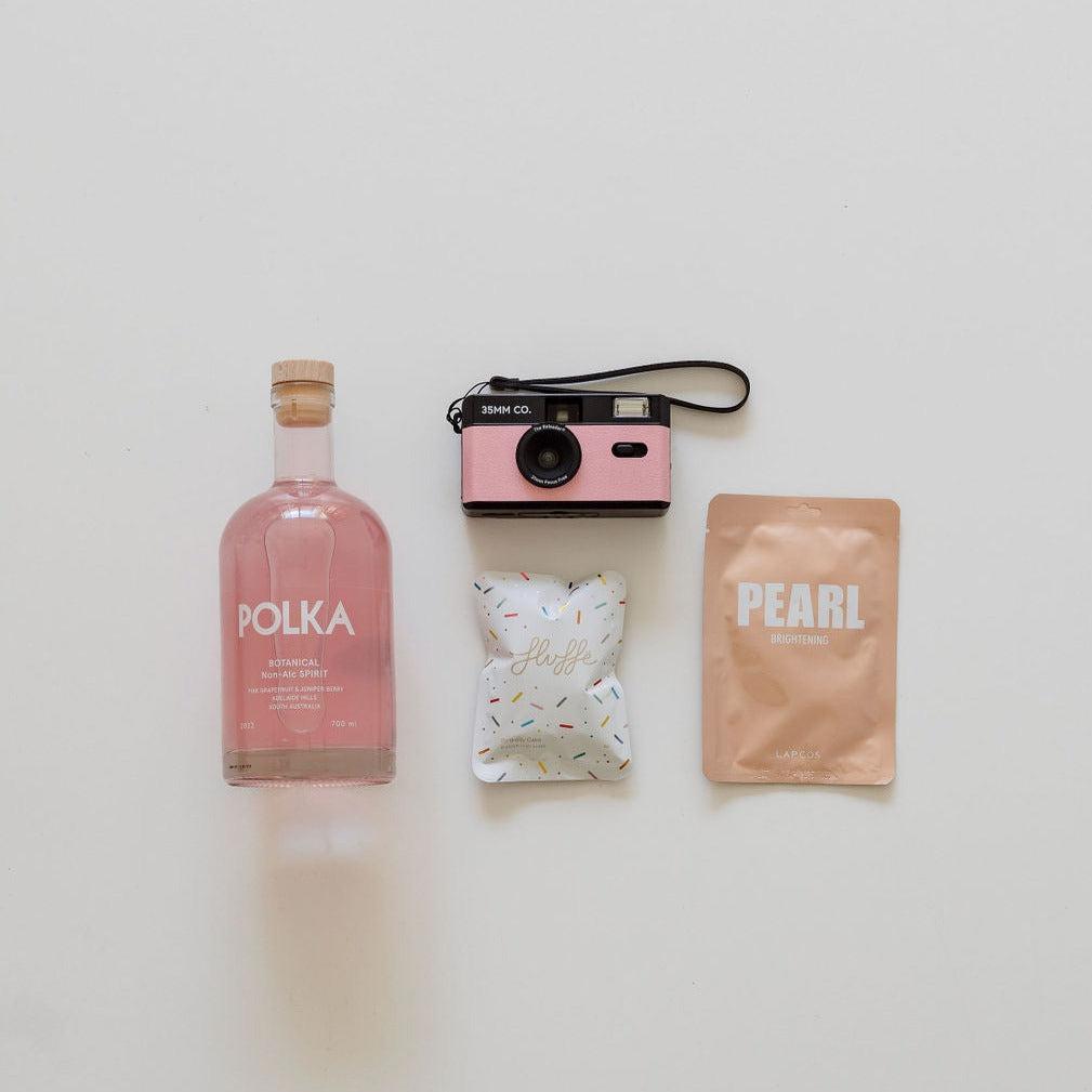 A pink bottle of capture the moment gin, a camera and a bag.