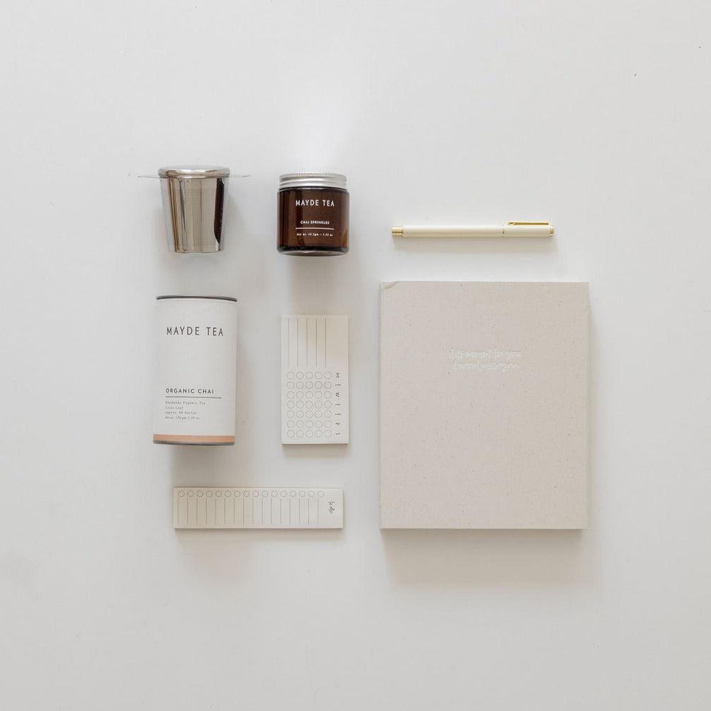 A chai time from biglittlegifting, pen, and a cup of coffee are laid out on a white surface.