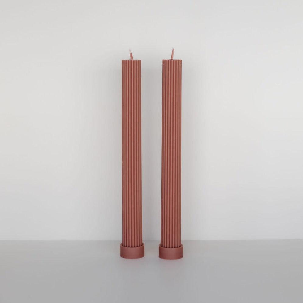 Two tall, ribbed, red Black Blaze soy wax column pillar candle duo standing upright on a plain white surface against a white background.
