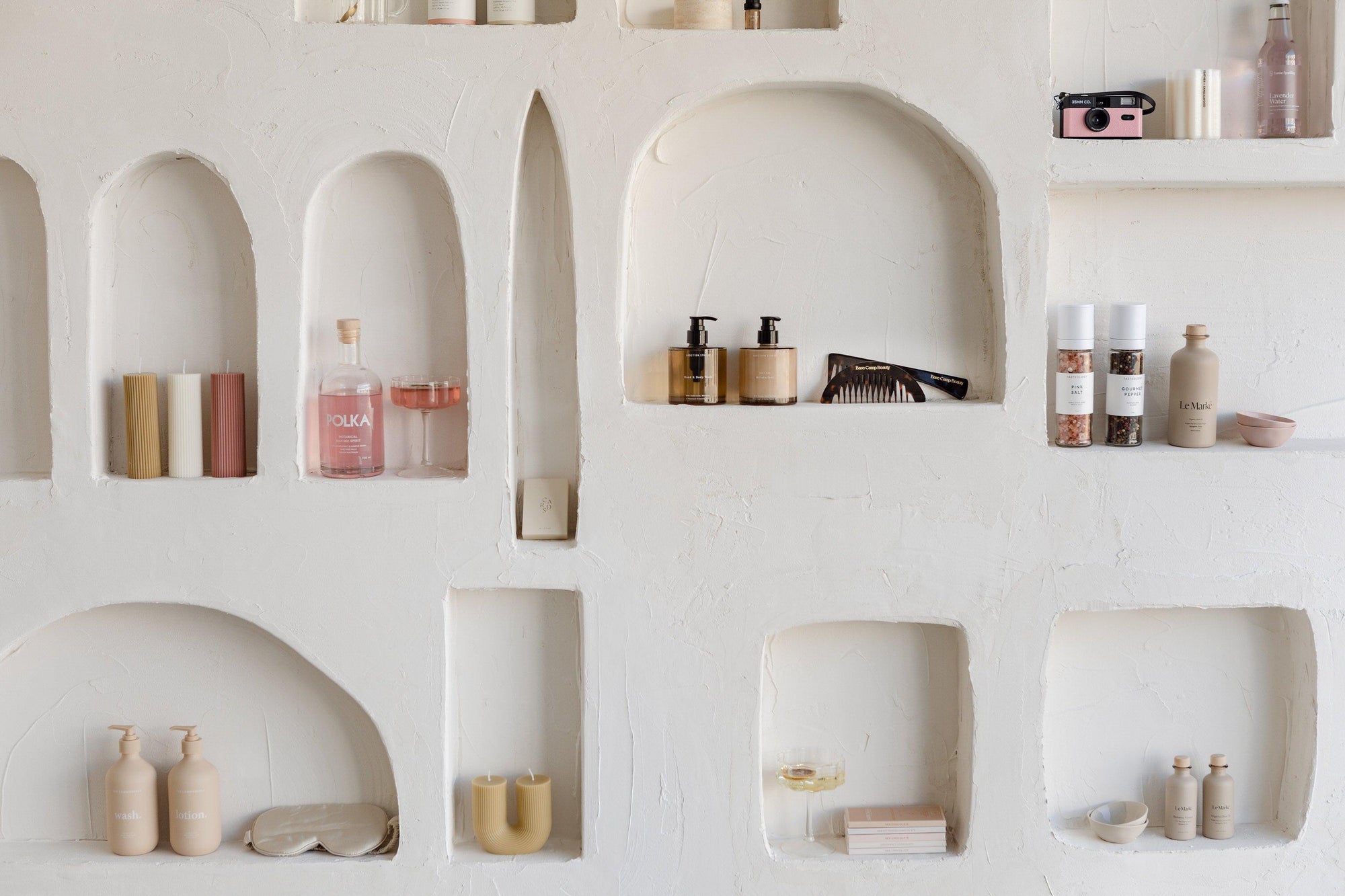 A white wall with shelves filled with BigLittleGifting's "Curate Your Own" cosmetics.