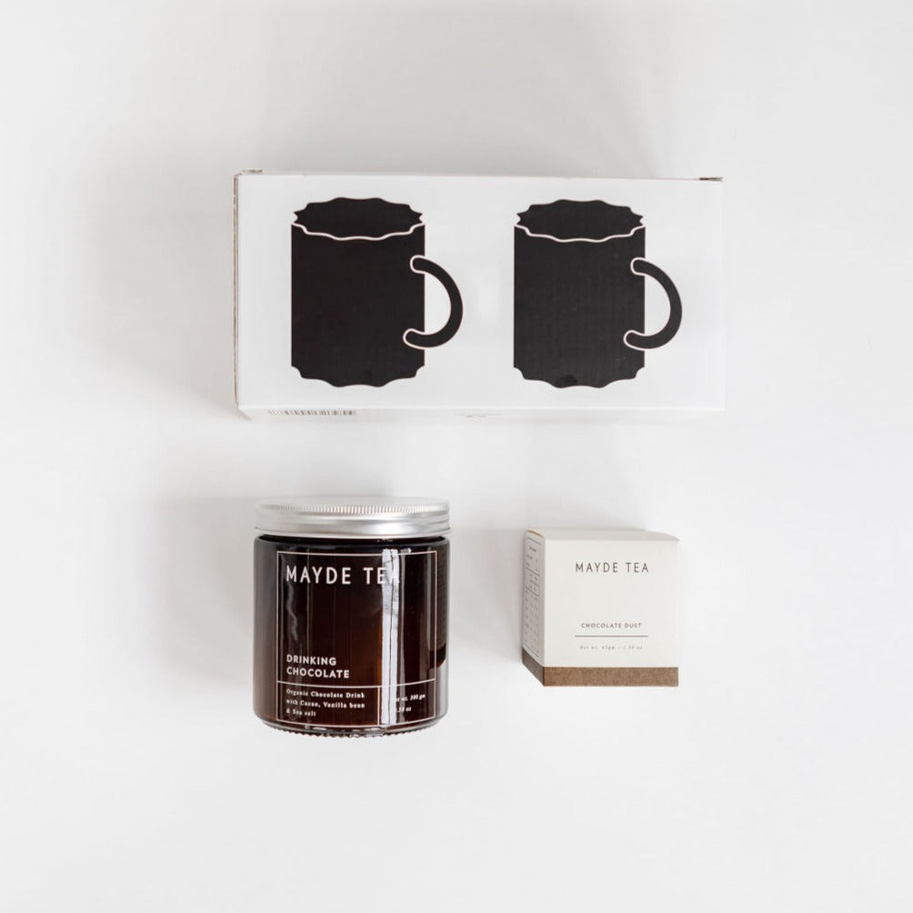 A cozy world of hot chocolate awaits in this curated gift box, featuring a Hot Chocolate Kit alongside a soothing candle on a table from biglittlegifting.
