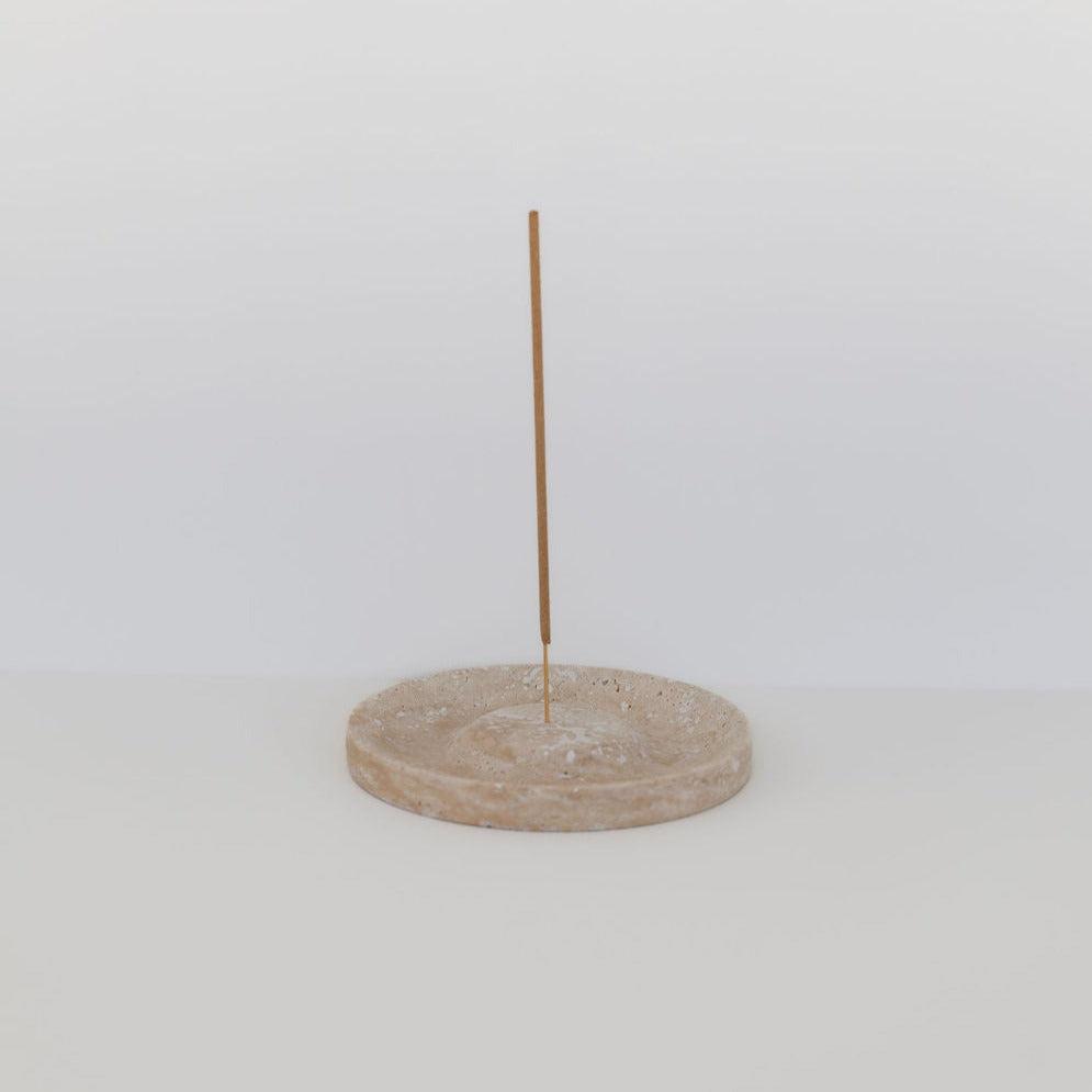 A single thin stick standing upright in a circular Addition Studio travertine stone base, placed against a plain white background.