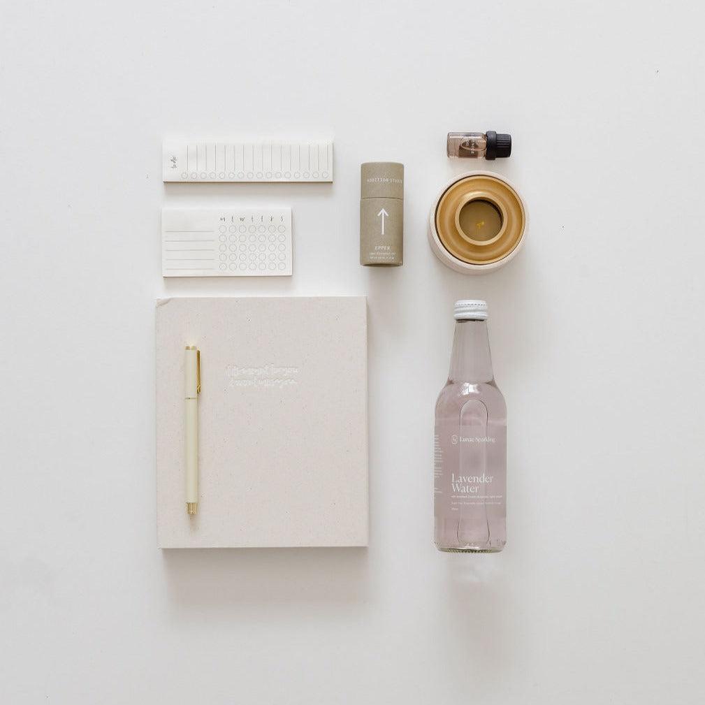 An entrepreneur vibes bottle of water, a pen, and a notebook are laid out on a white surface.