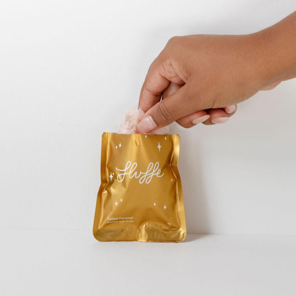 A vegan hand holding a gold foil bag filled with Fluffe fairy floss | salted caramel.
