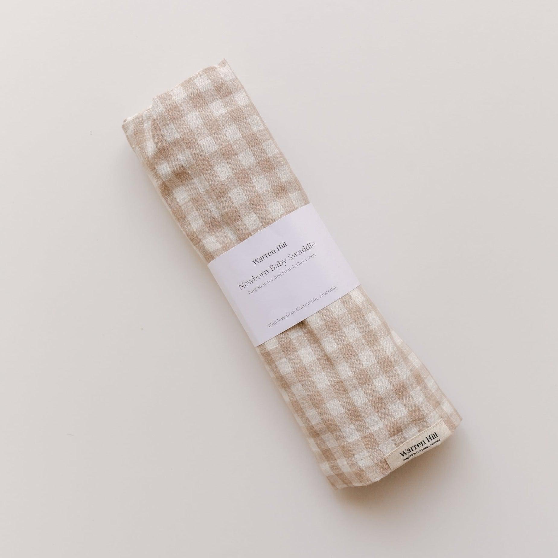 A beige and white gingham Warren Hill French linen baby swaddle on a white surface.