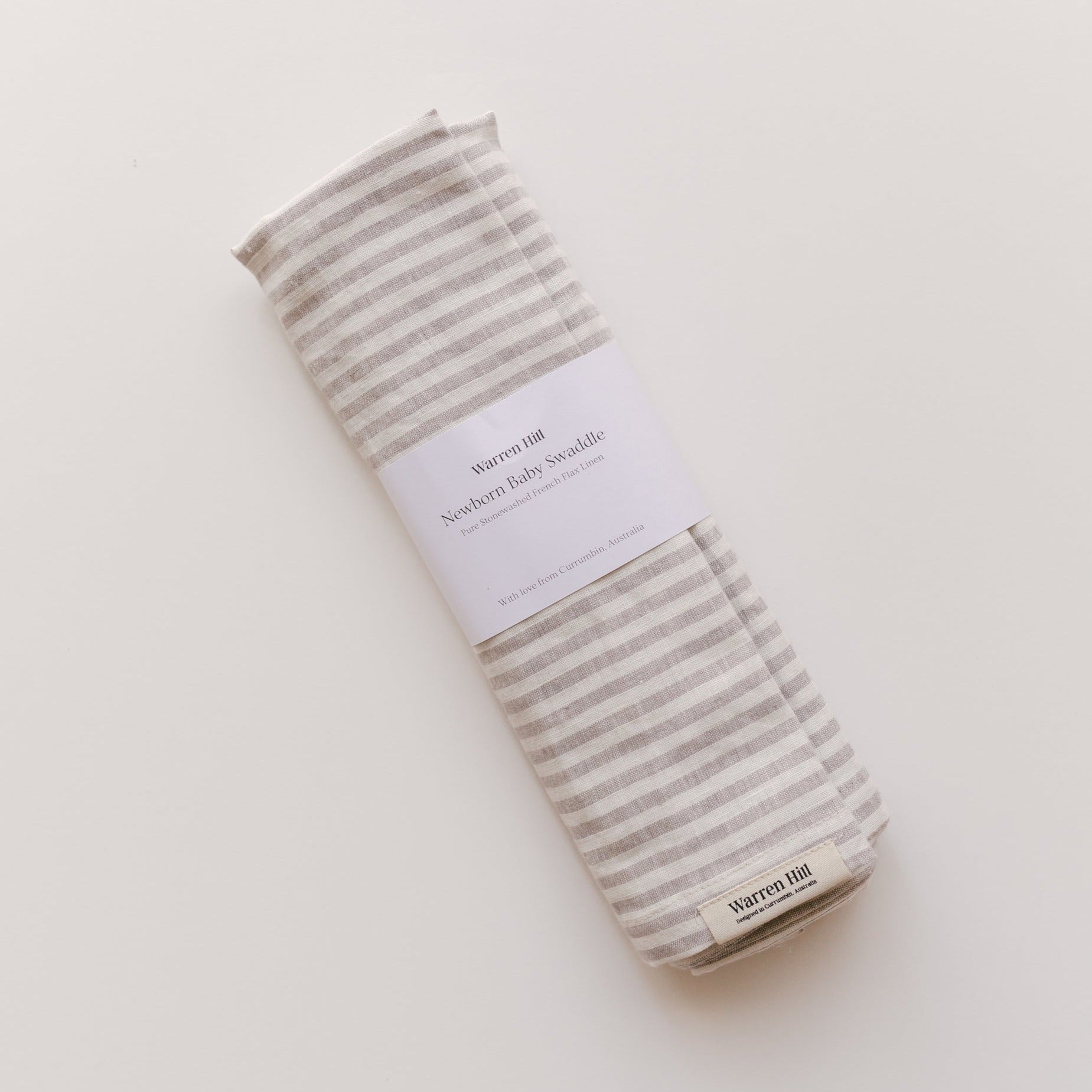A French linen baby swaddle in grey stripe on a white surface by Warren Hill.