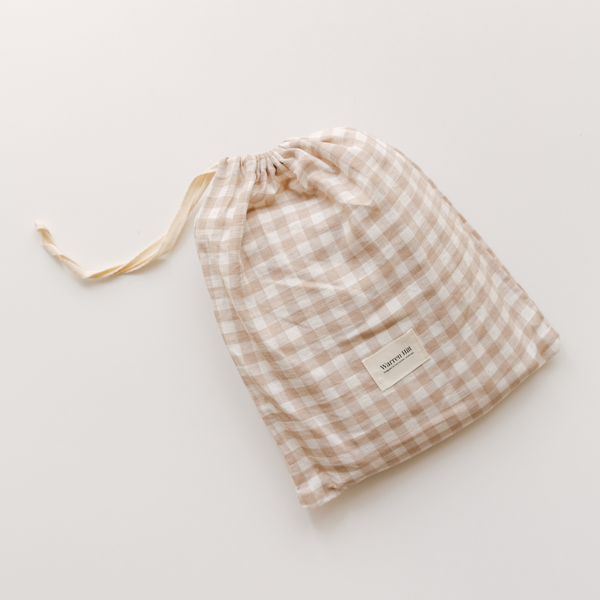 Light beige and white checkered drawstring bag made from Warren Hill French linen fitted cot sheet, with a label on a plain white background.