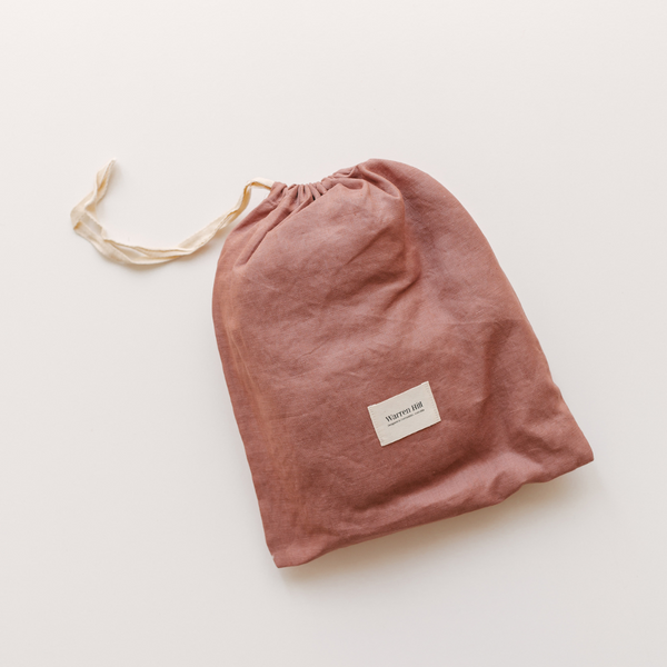 A pink drawstring bag on a white surface, perfect for storing Warren Hill french linen fitted cot sheets in smoke pink.