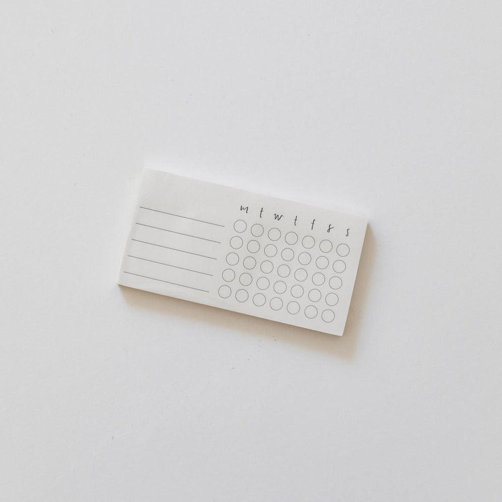 A white habit tracker sticky note on a white surface, from Emma Kate Co.