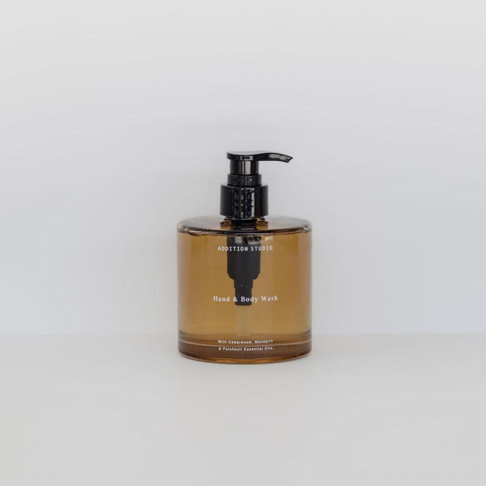 Amber glass bottle of Addition Studio hand & body wash with black pump, against a plain white background.