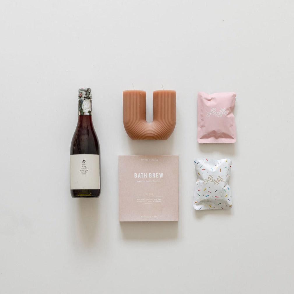 A gift box containing a bottle of "here's to you" wine from "biglittlegifting" is laid out on a white surface, promoting relaxation.