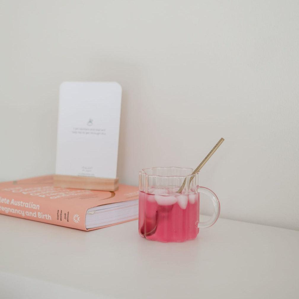 A cup of Hydramama® Watermelon + Lime by Mini+Me liquid next to a book on a shelf.
