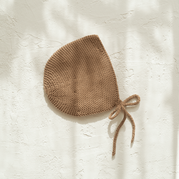 An Illoura the Label knitted beanie, made from organic cotton, hanging on a wall.