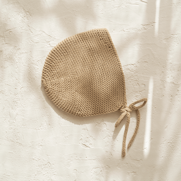 An Illoura baby bonnet in olive hanging on a wall.