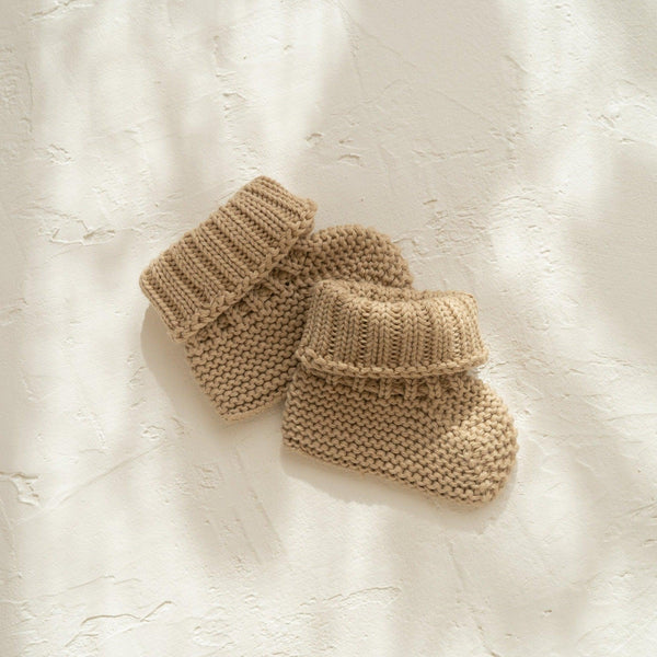 A pair of Illoura the Label organic cotton baby booties in illoura baby booties | olive on a white surface.