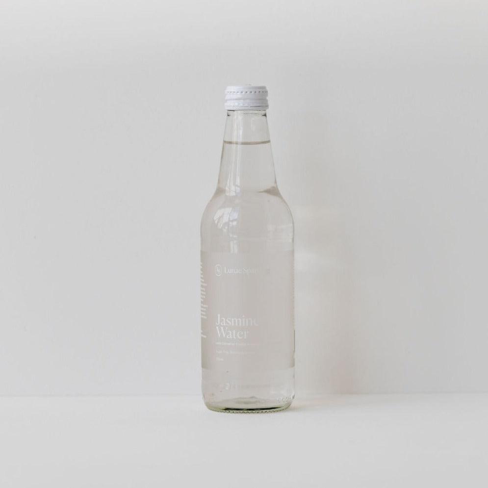 A positively charged bottle of Lunae Sparkling jasmine water, sugar-free, sitting on a white surface.
