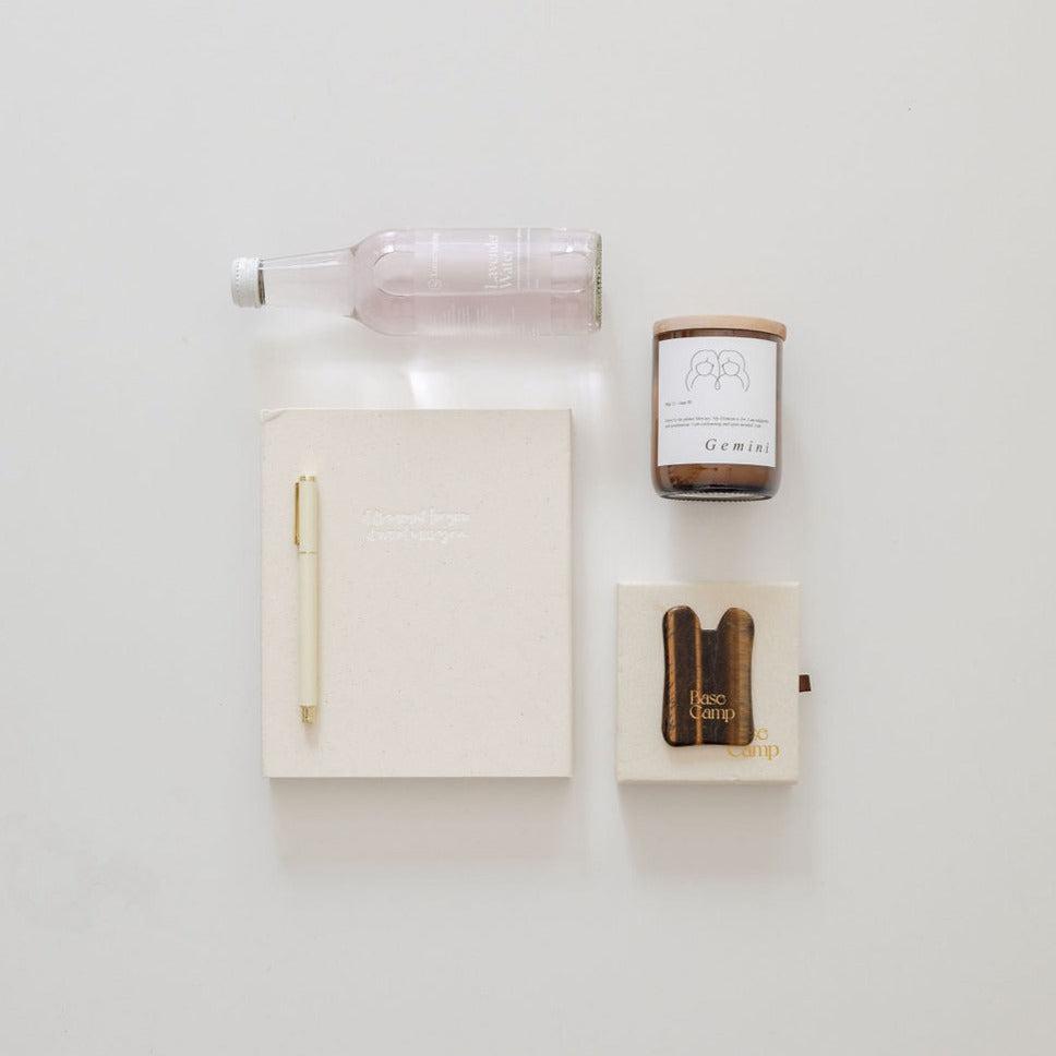 A manifesting moments notebook, a pen and a bottle of water on a white surface by biglittlegifting.