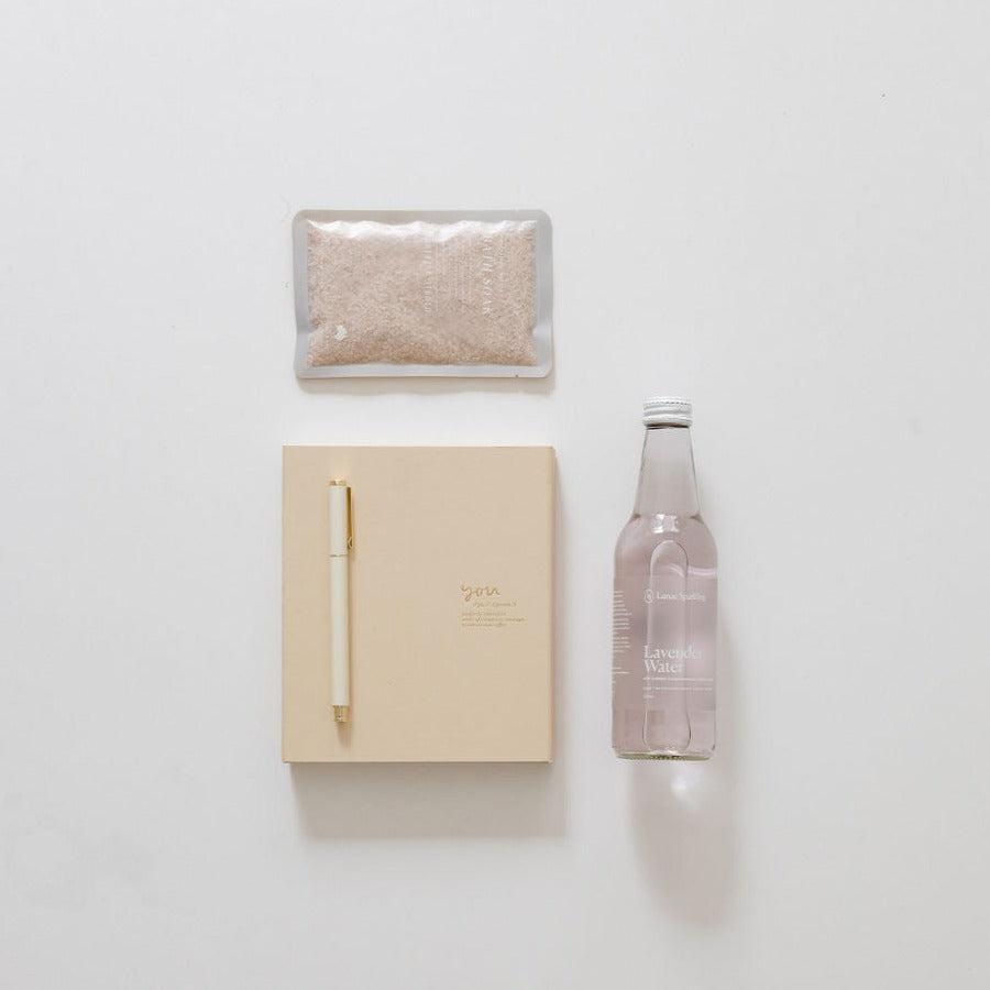 A bottle of moments for you water and a notepad from biglittlegifting on a white surface, creating a serene and reflective atmosphere.