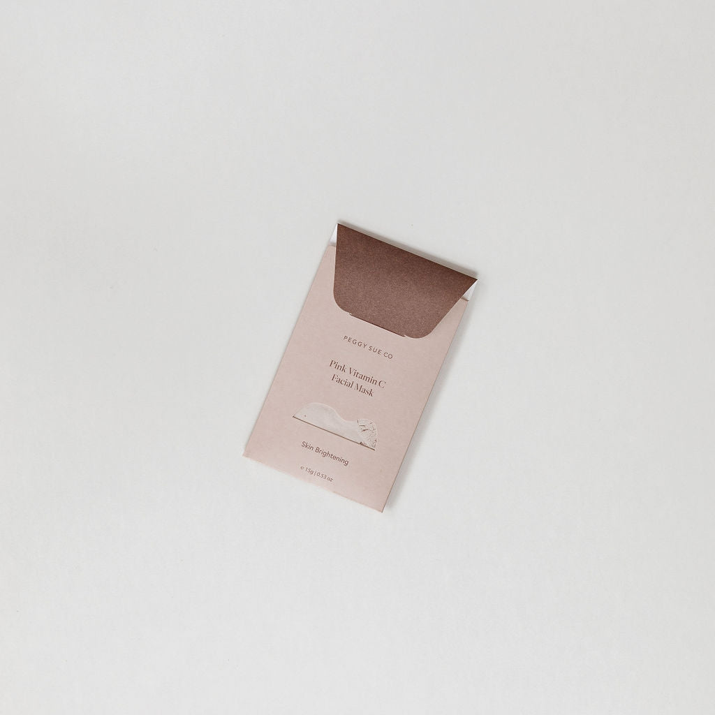 A small brown Skin Brightening Facial Mask by Peggy Sue Co. envelope sitting on top of a white surface.