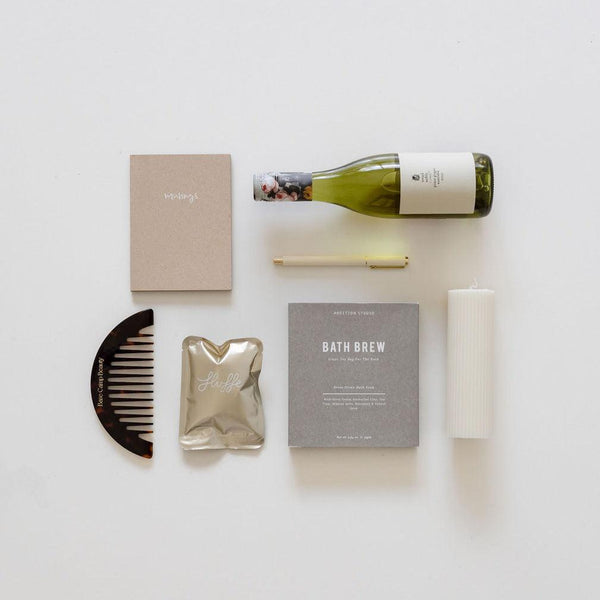 A bottle of savour the moment wine and other items are laid out on a white surface. (Brand Name: biglittlegifting)