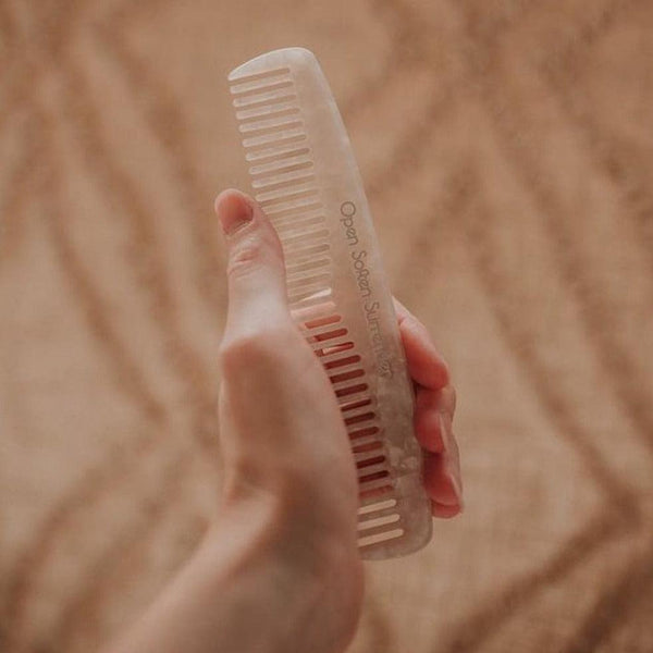 A person holding a Seasons of Mama Birth Comb on top of a rug.