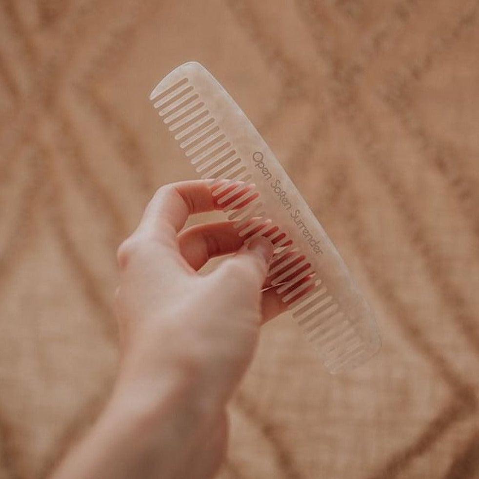A person holding a Seasons of Mama Birth Comb on top of a rug.