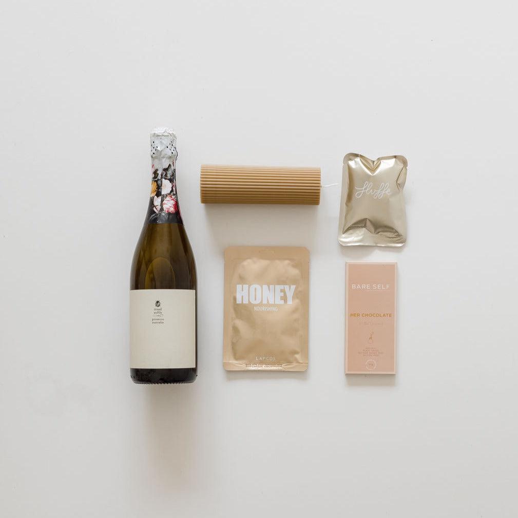 A bottle of sips & treats from biglittlegifting, chocolate, and other items are laid out on a white surface.