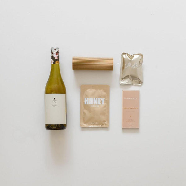 A bottle of sips & treats from biglittlegifting and other items are laid out on a white surface.
