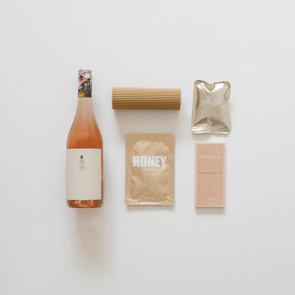 A bottle of sips & treats from biglittlegifting and other items are laid out on a white surface.