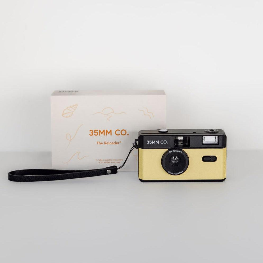 A yellow 35mm camera with a black strap in front of a box, the reloader® reusable film camera.