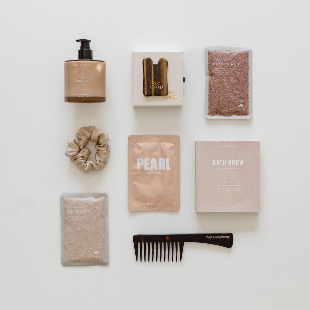 A collection of self-care cosmetics and a comb from "biglittlegifting's ultimate pampering session" on a white surface, perfect for relaxation or as a thoughtful gift.