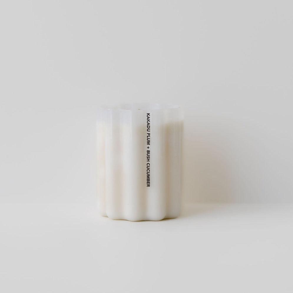 A Fazeek wave candle in the scent of kakadu plum & bush cucumber sitting on a white surface.
