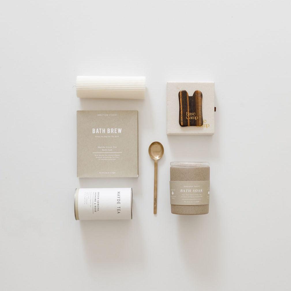 A wellness & warmth gift box from biglittlegifting with a set of soaps, a spoon, and a candle on a white surface, promoting relaxation and well-being.