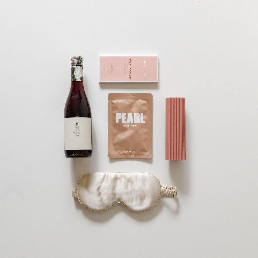 A bottle of wine & unwind from biglittlegifting and other items are laid out on a white surface.