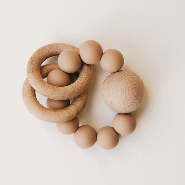 A collection of Dove & Dovelet Wooden Silicone Teethers made from BPA-free silicone beads and a sphere surrounded by a group of eggs on a white surface, meeting Australian Toy Safety Standards.