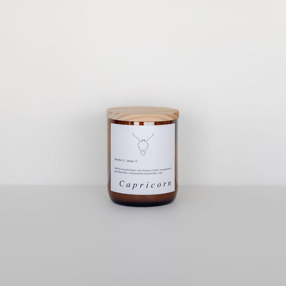 A Zodiac Candle labeled "Capricorn" with a simple deer graphic on the label, made from soy candle wax, placed against a plain white background by The Commonfolk Collective.