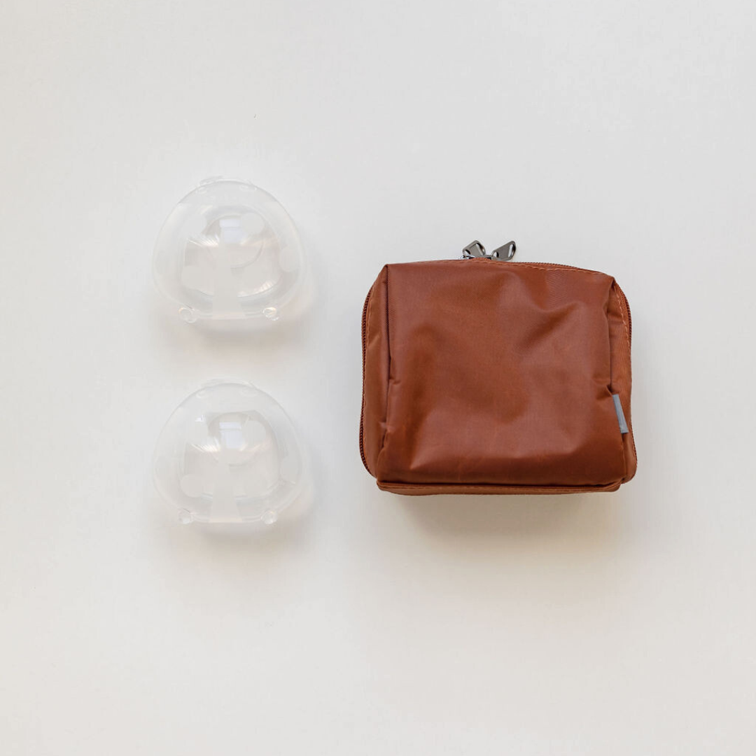 A brown bag with two Haakaa Ladybug silicone Breast Milk Collectors with Storage Bag on it.