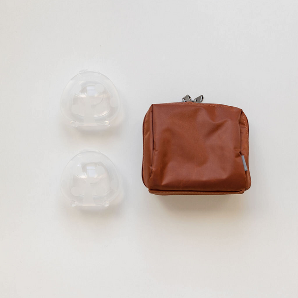 A brown bag with two Haakaa Ladybug silicone Breast Milk Collectors with Storage Bag on it.