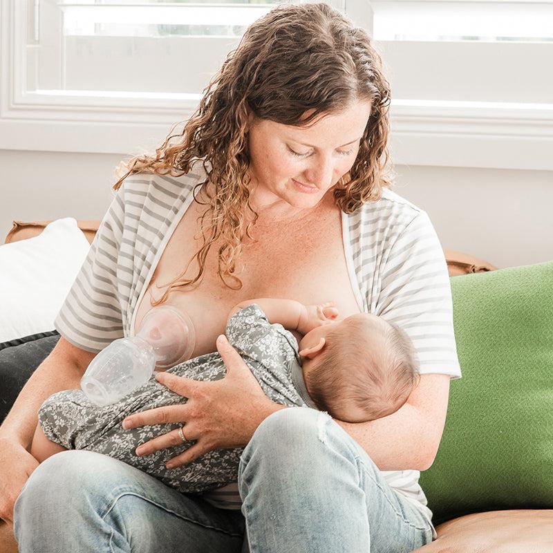 A woman breastfeeds her baby using the Haakaa Silicone Breast Pump 100ml | Gen 1 on a couch.